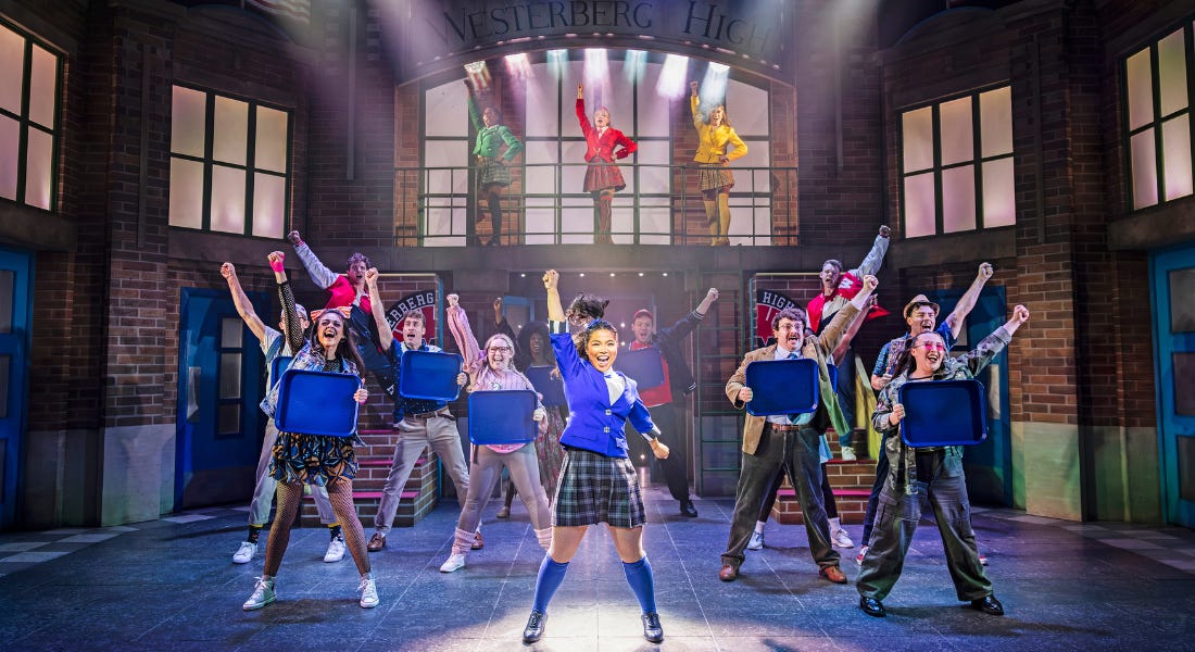 A group of people on stage with their fists in the air, in a school setting A group of people on stage with their fists in the air, in a school setting