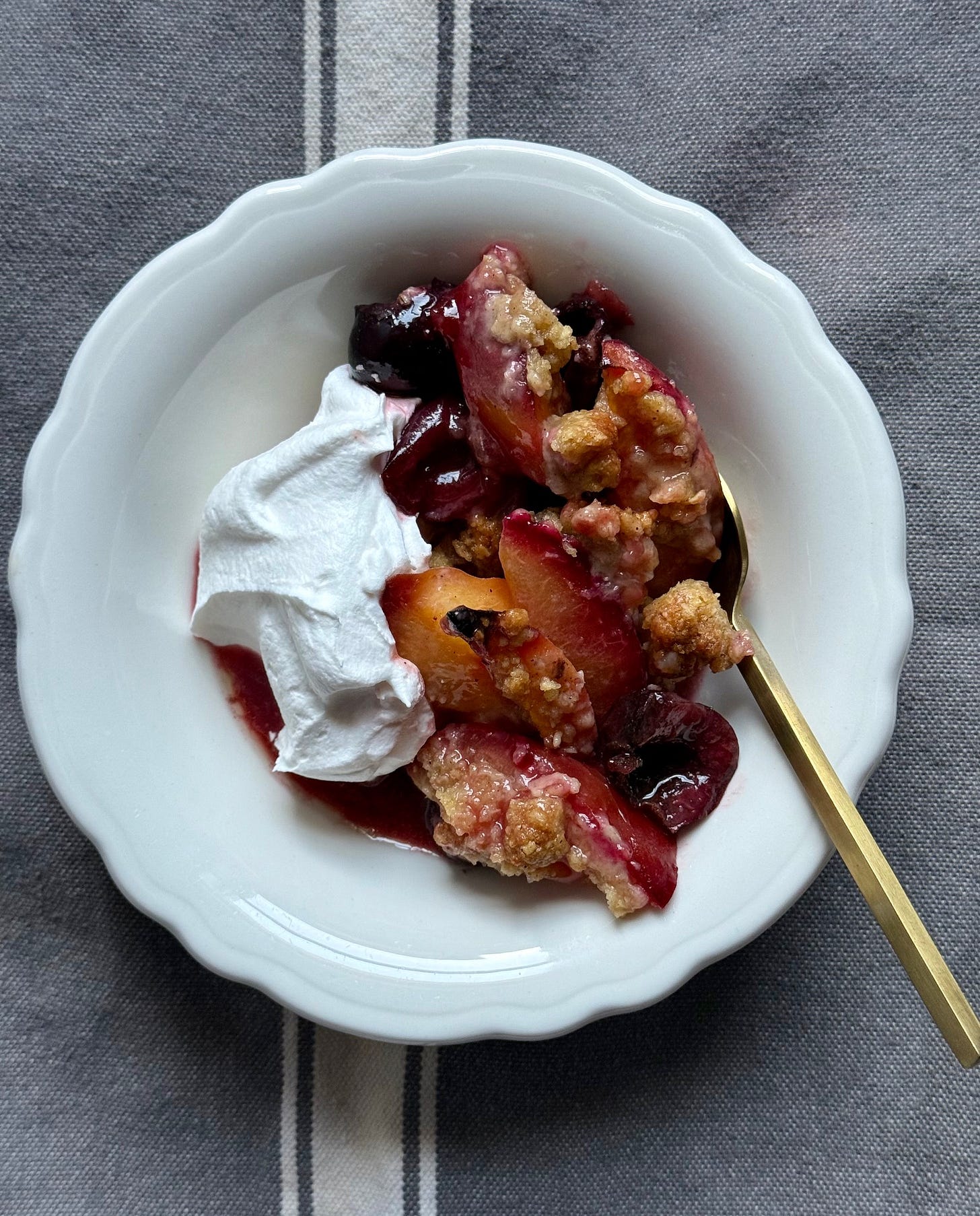 a white bowl of roasted fruit crumble with whipped cream. Studio Delicious.com 