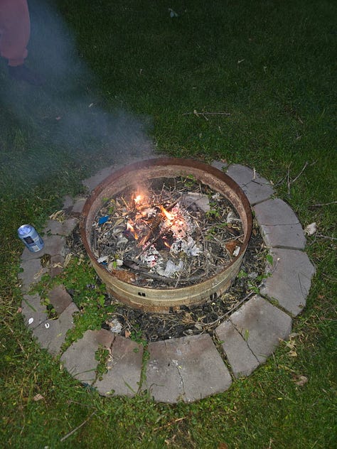 folded papers on top of jean covered notebook, crumpled paper and a knee, a small fire burning in a fire pit.