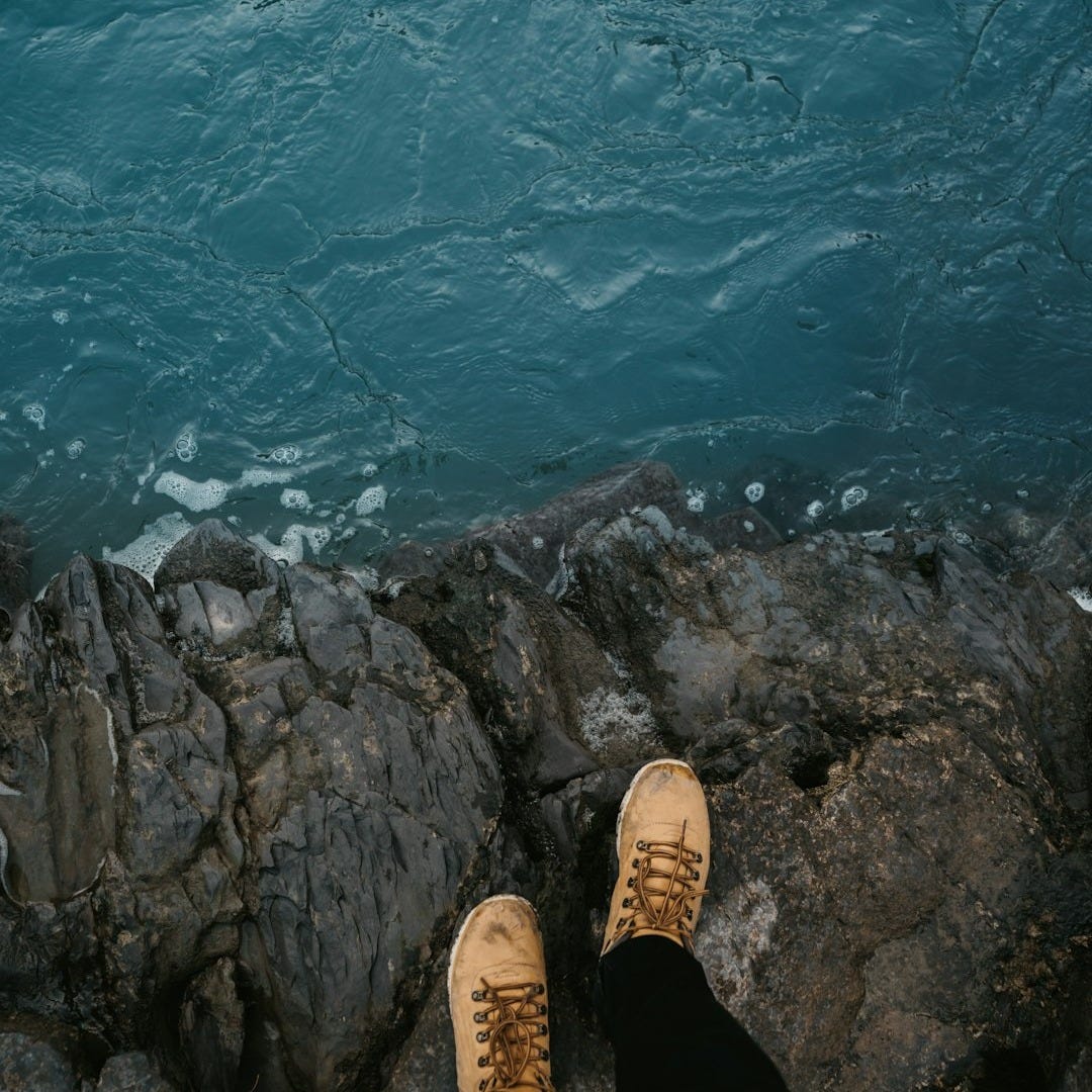 person in black pants and brown shoes standing on rocky cliff