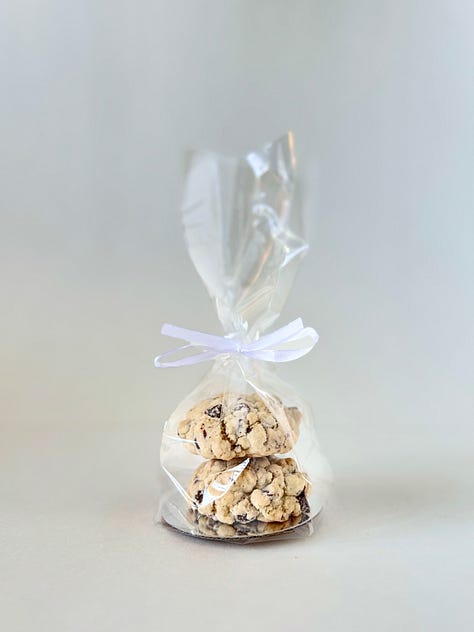 1: Two chocolate chip cookies side by side, the left propped up the right. 2: Two chocolate chip cookies, one stacked on top of the other. 3: two chocolate chip cookies stacked in a clear plastic bag tied with a white bow.