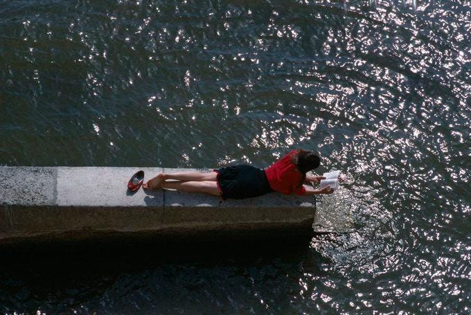 This may contain: a woman laying on the edge of a concrete pier next to water with her legs crossed