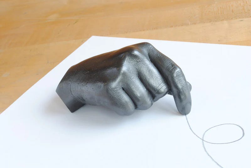 A graphite casting of the artist's hand. The grey hand is posed as if holding a pencil or pointing. The pointer finger has drawn a looping line on the paper.