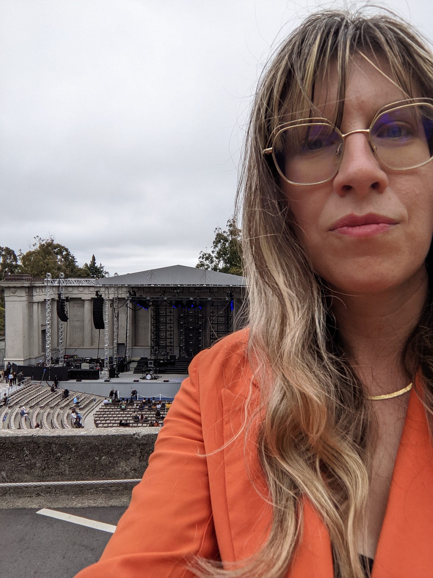 photo of Sarah Wheeler, a white woman in an orange blazer at an outdoor concert photo of Sarah Wheeler, a white woman in an orange blazer at an outdoor concert