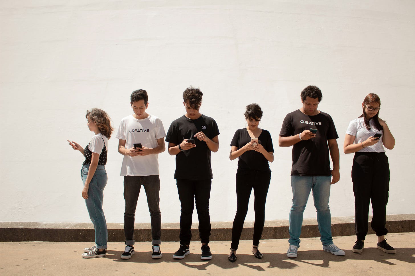 Six people stand outdoors while looking at their smartphones, illustrating how social media feeds capture individual attention. Six people stand outdoors while looking at their smartphones, illustrating how social media feeds capture individual attention.
