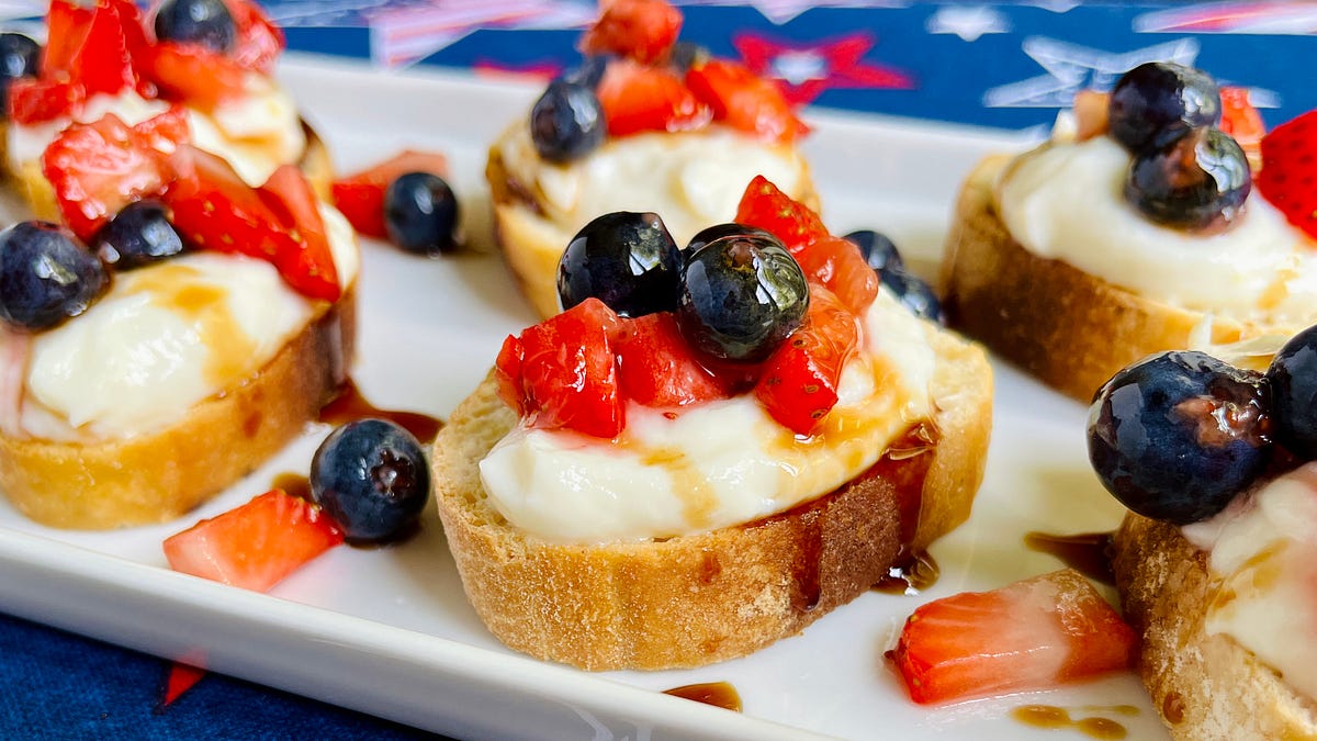 Slices of bruschetta topped with whipped ricotta and fresh berries on a white platter. 
