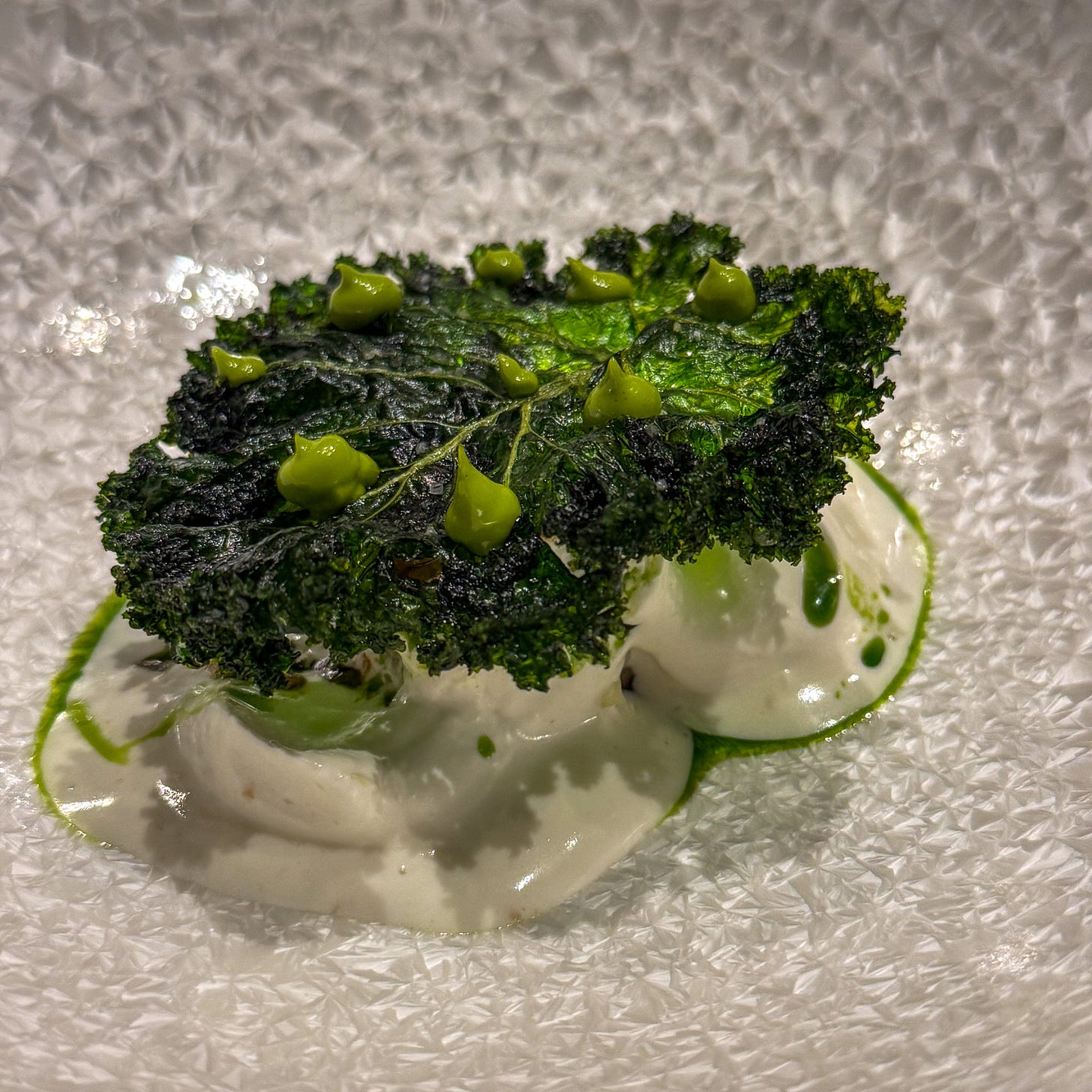 Kohlrabi prepared pastrami-style topped with charred kale leaves and green herb oil dots over coconut cream sauce at Mantra restaurant