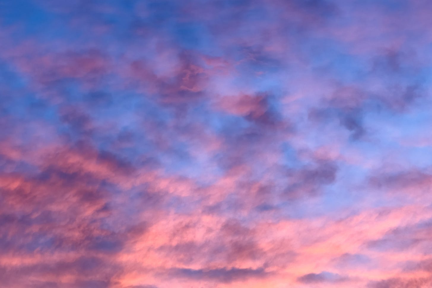 Blue sky with pink, and grey clouds formed by the setting sun