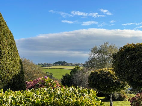 two photos of huge cliffs and pebbly beaches, a flat sand and water shot, a lush green garden with bushes, a close up of hydrangeas, a view over a green garden with white clouds on the blue sky and green hills in the distance