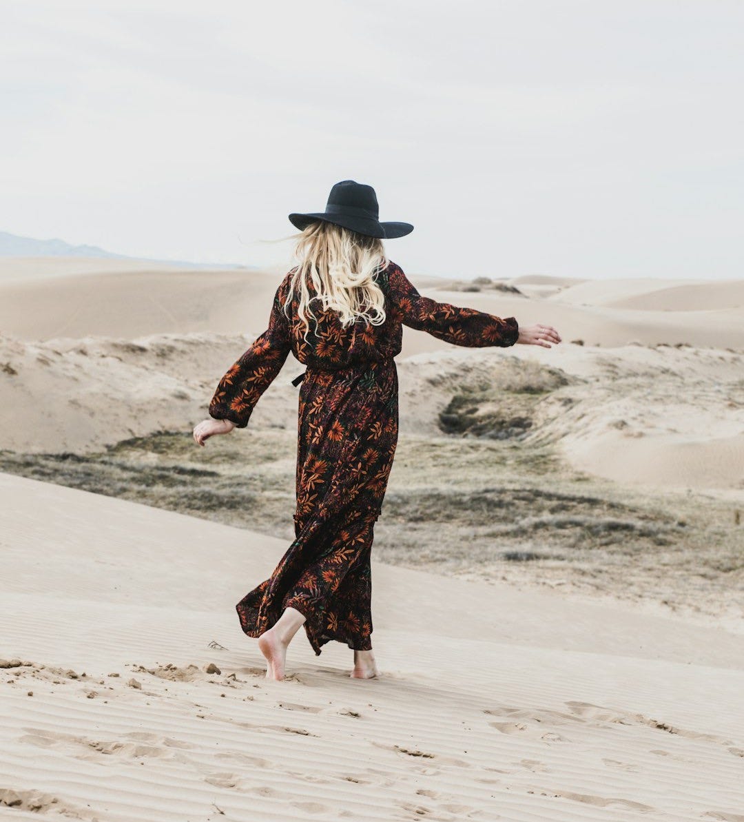 photo of person wearing brown and orange floral maxi dress walking barefooted along deserted land photo of person wearing brown and orange floral maxi dress walking barefooted along deserted land