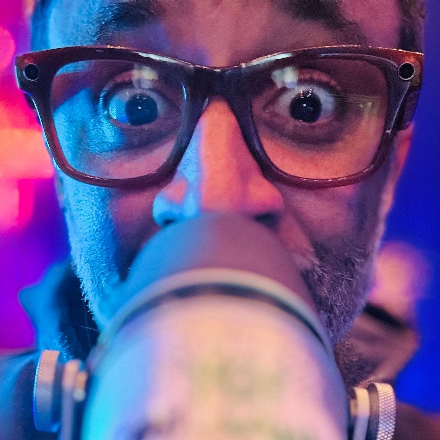Nate, staring down the barrel of his microphone at the camera, eyes wide in glasses.