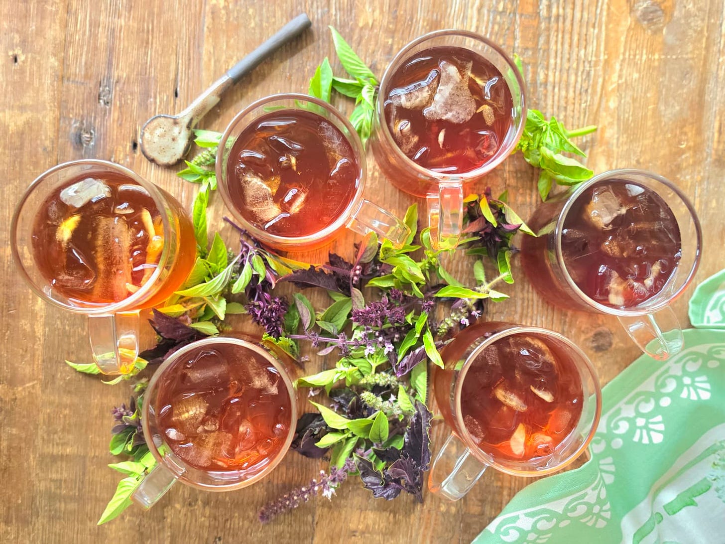 6 glasses of iced tea with fresh basil trimmings, a spoon, and a kitchen towel on a table 6 glasses of iced tea with fresh basil trimmings, a spoon, and a kitchen towel on a table