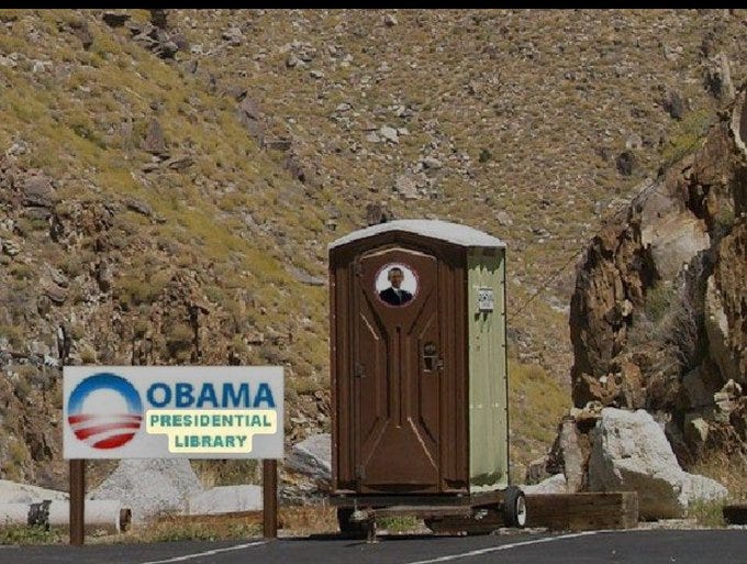 A portable toilet with a photo of Barack Obama on it, situated outdoors in a rocky, mountainous area. A sign nearby reads "Obama Presidential Library" with the Obama campaign logo.