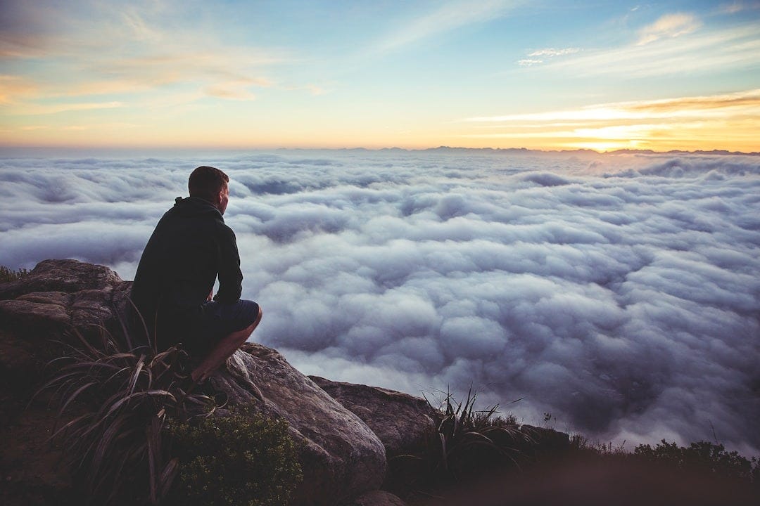 man sitting on gray rock while staring at white clouds man sitting on gray rock while staring at white clouds