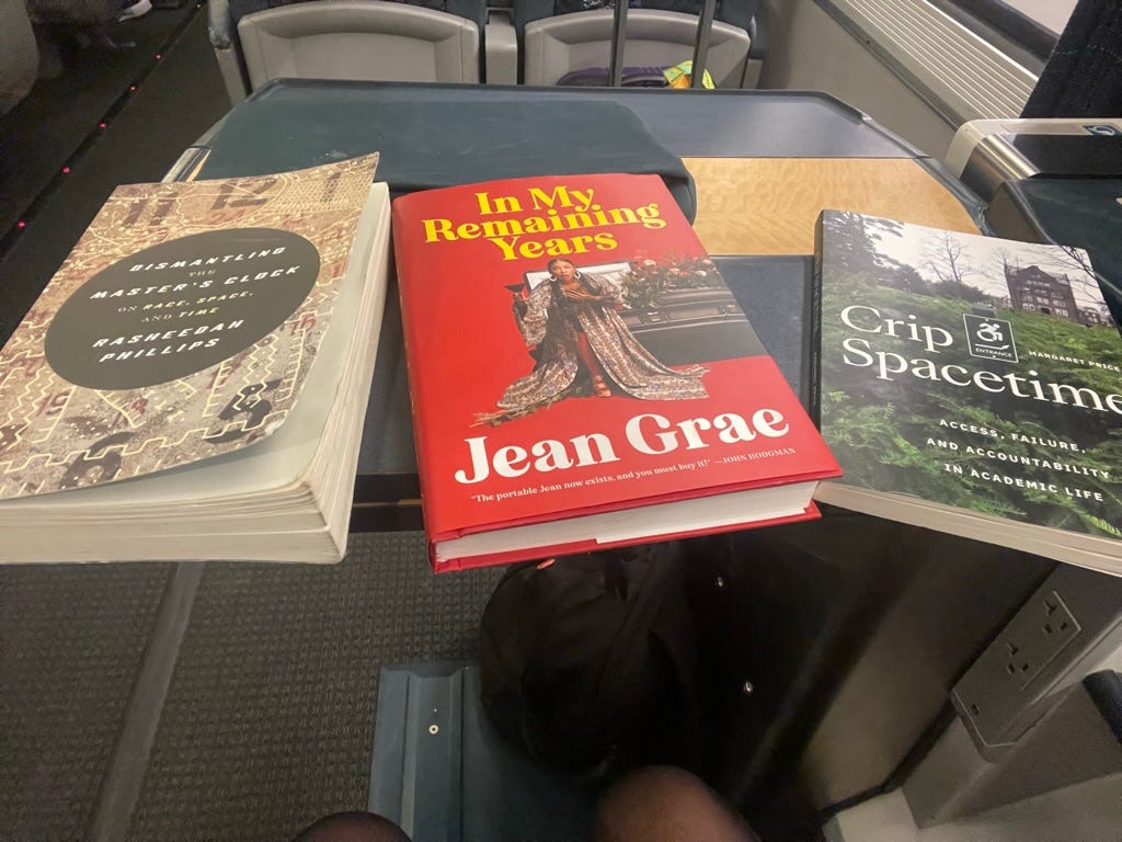 photo of Dismantling the Master's Clock by Rasheedah Phillips, In My Remaining Years by Jean Grae and Crip Spacetime by Margaret Price, on a fold out table on Amtrak