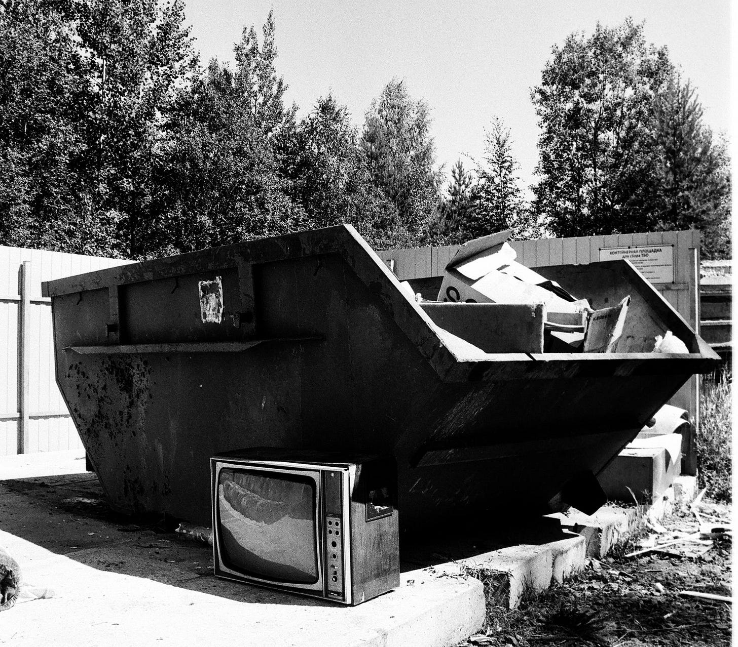 Black and white photo of a dumpster with trash around it