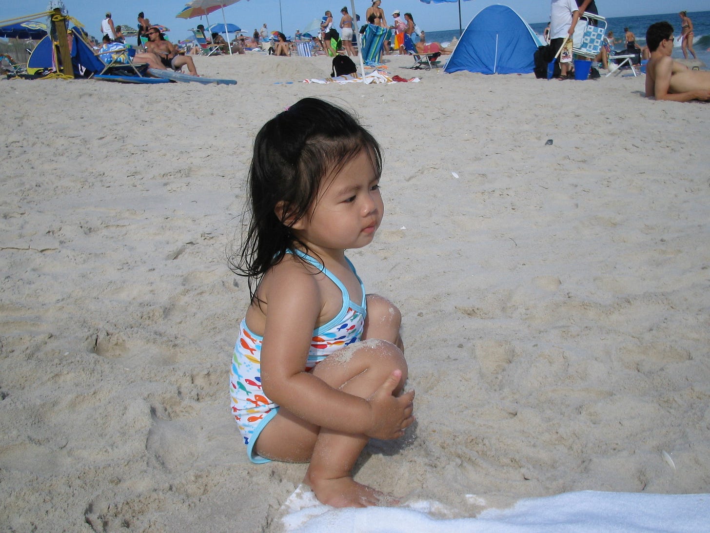 A baby Lea at the beach, squatting in the sand an staring wistfully at the ocean.
