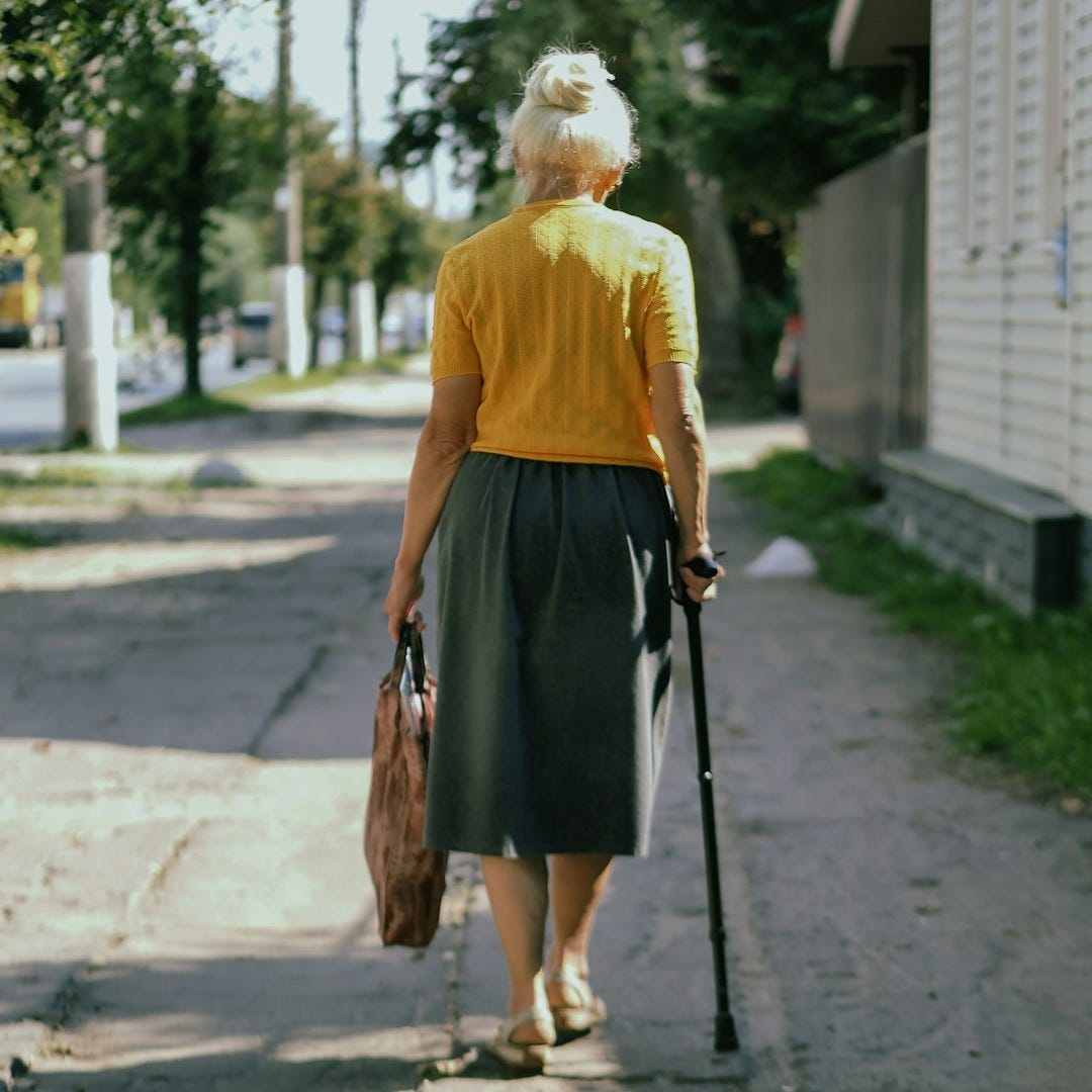 a woman walking down a sidewalk with a cane