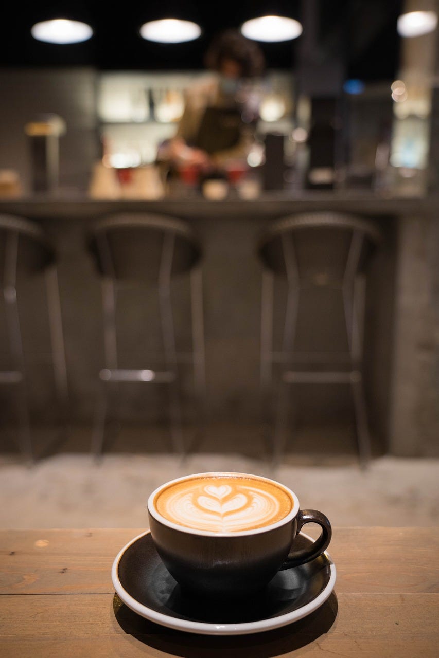 Blurred cafe background, wooden table in foreground with a coffee cup with beautiful foam art