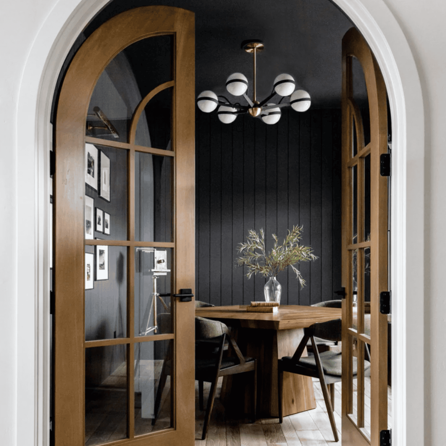 Sherwin Williams tricorn black painted wall with a dining room table in front of a door and gallery wall.