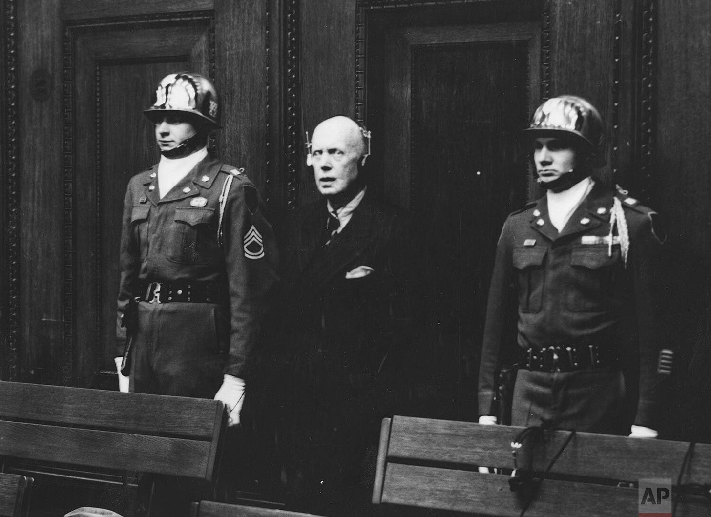 Heinrich Lammers receives a 20-year prison sentence, flanked by U.S. Army honor guards Sgt. Thomas H. Andress and Pvt. Leen J. Baran, members of the 16th Infantry Regiment, at Nuremberg.