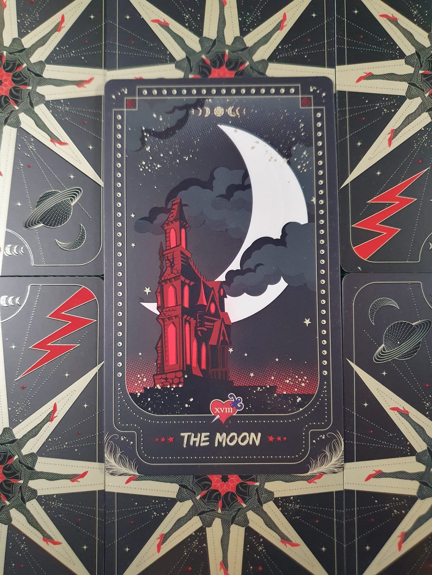 The Moon card from a gothic-themed tarot deck, featuring an illuminated red castle beneath an enormous white crescent moon, surrounded by dark clouds and stars against a midnight sky. The Moon card from a gothic-themed tarot deck, featuring an illuminated red castle beneath an enormous white crescent moon, surrounded by dark clouds and stars against a midnight sky.