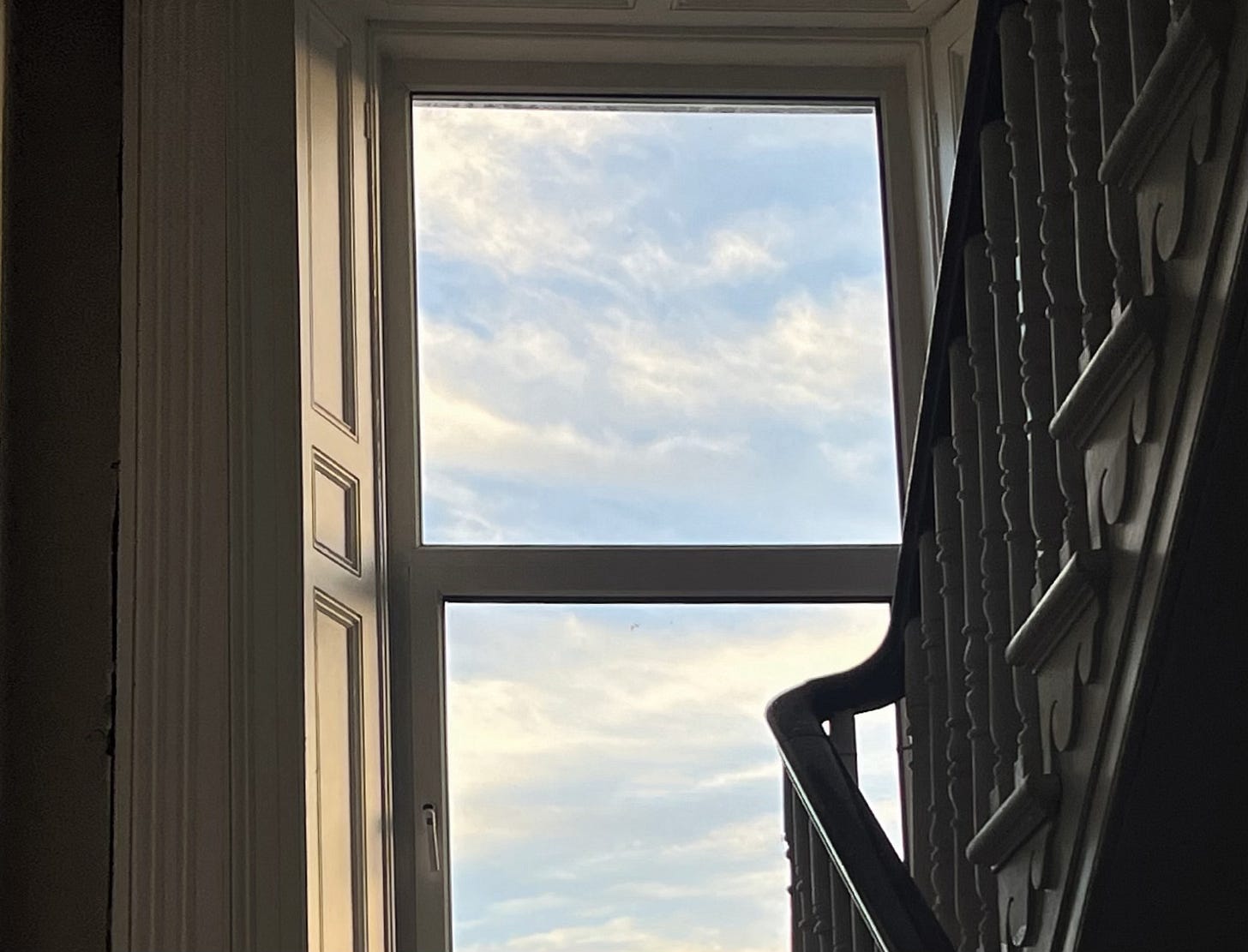 A view of clouds out of a stairwell’s landing window.