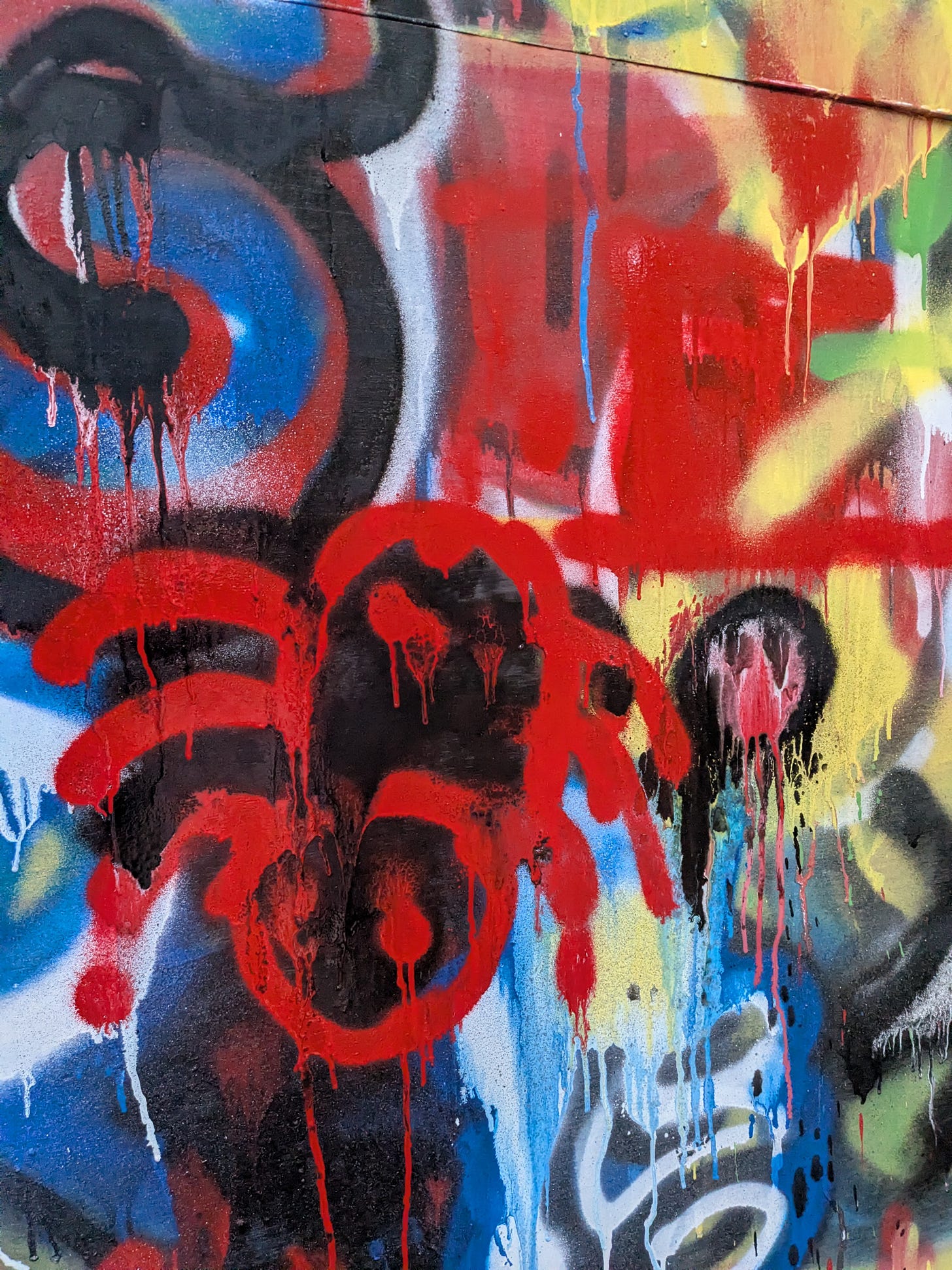 A closeup of a spray-painted red spider outline on top of other spray painted graffiti style art on plywood boards