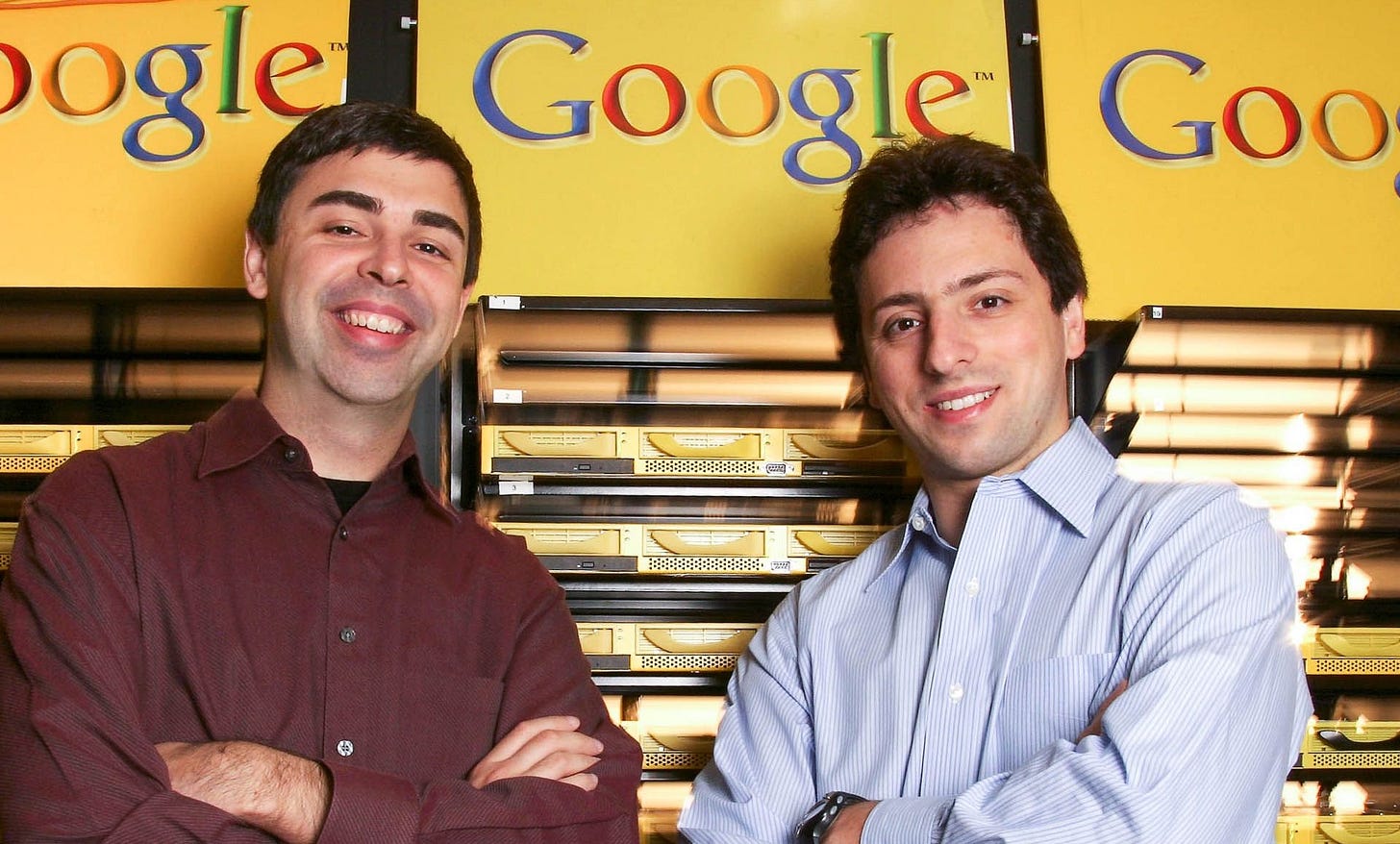 Larry Page and Sergey Brin stand with arms crossed inside Google headquarters