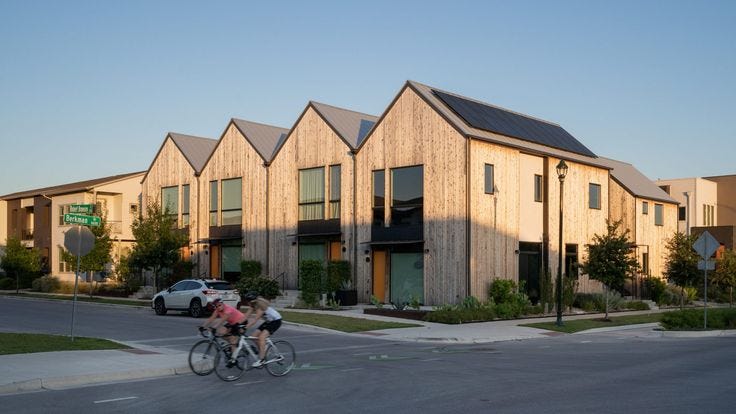 This may contain: two people riding bikes down the street in front of some buildings with solar panels on them