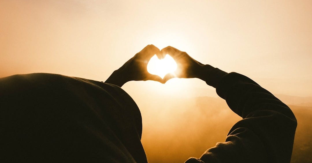 person doing heart shape hand with sun light passing thru