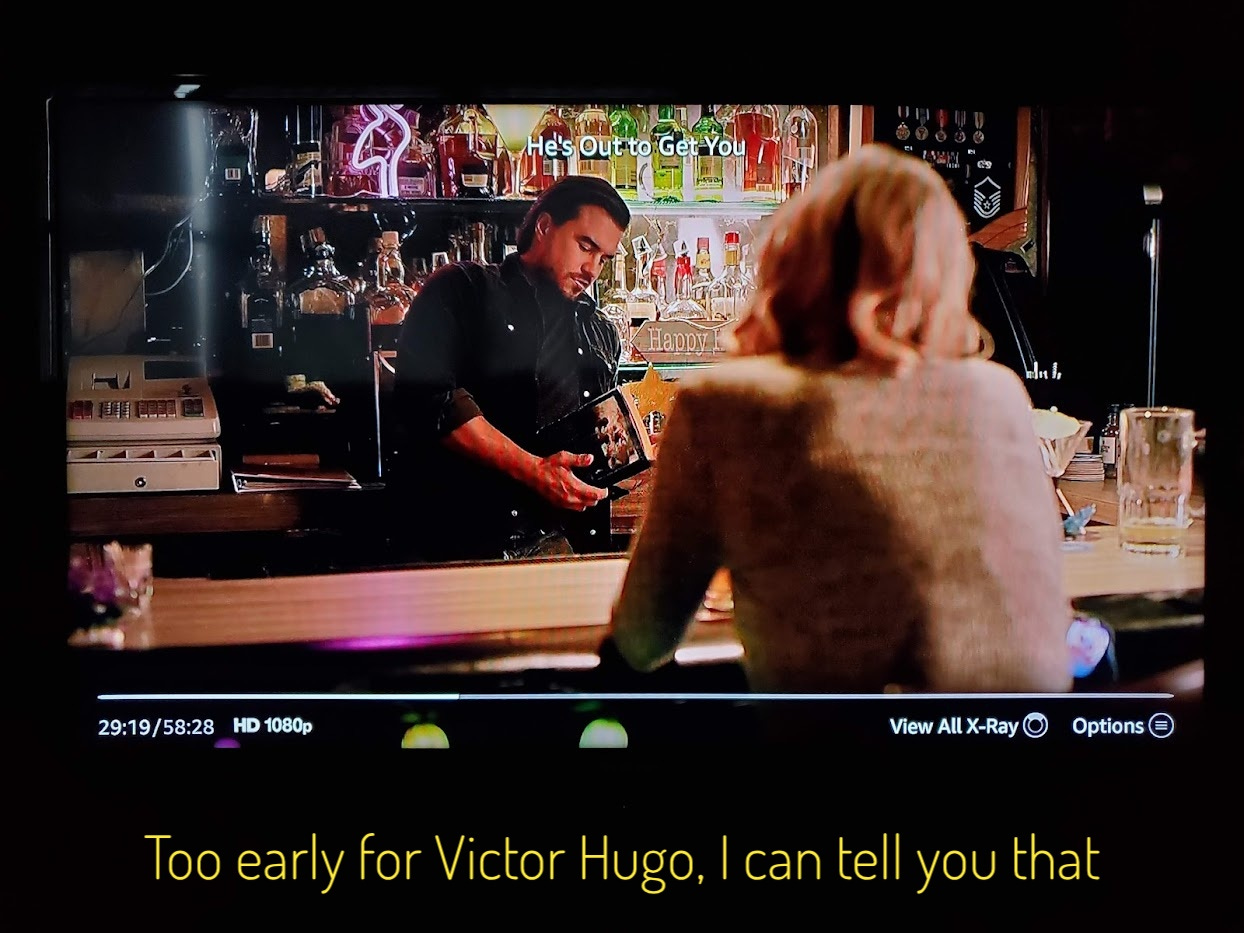 Duke the bartender leaning on the back of the bar reading a thick book, captioned "Too early for Victor Hugo, I can tell you that"