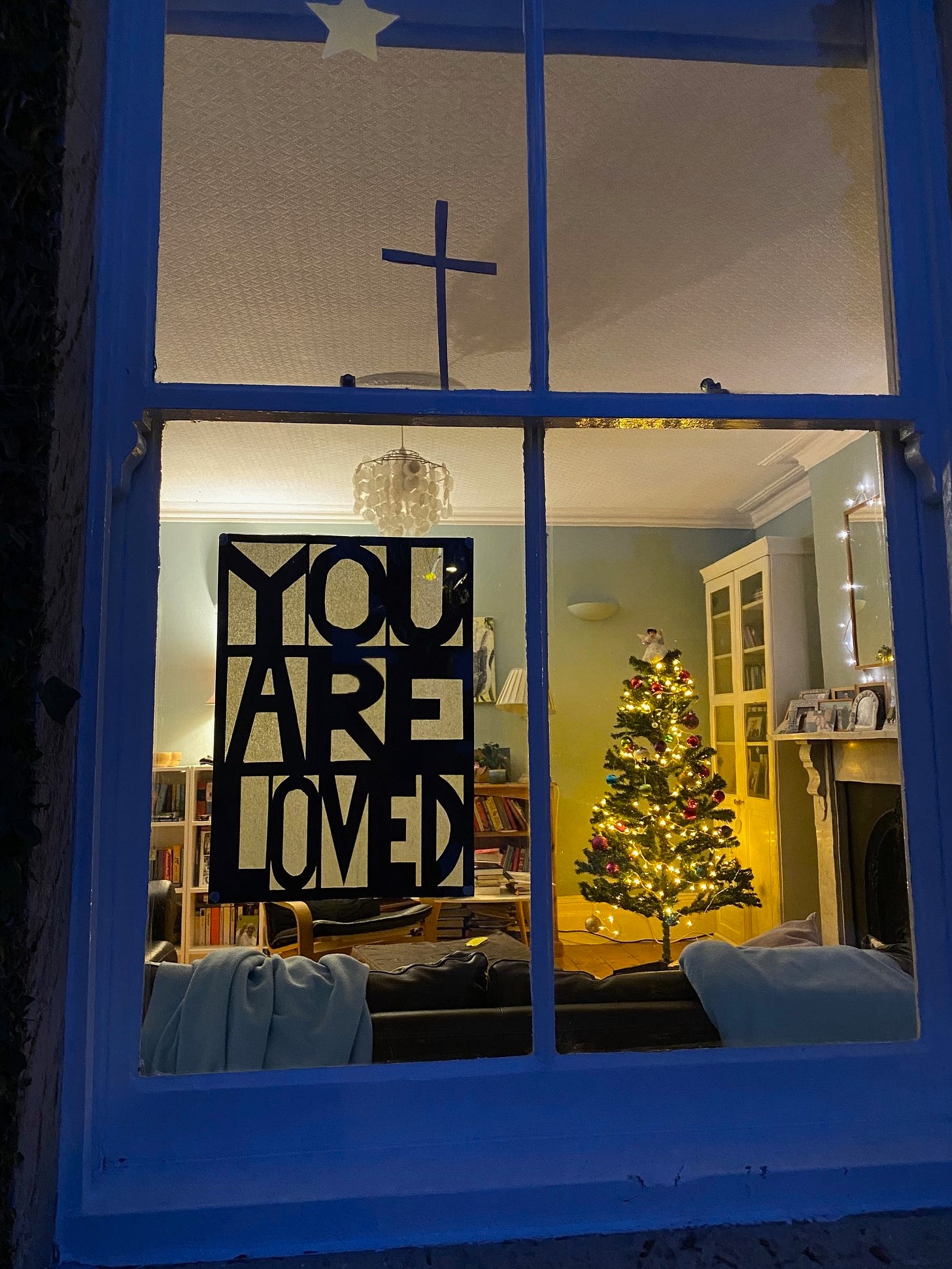 A sign saying You Are Loved affixed to a window through which can be seen a Christmas tree A sign saying You Are Loved affixed to a window through which can be seen a Christmas tree