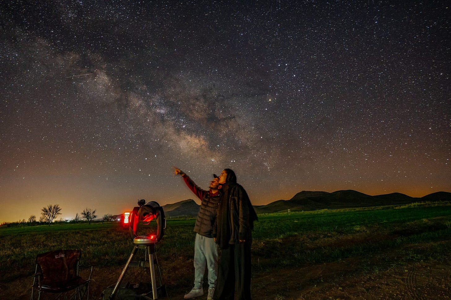 two people looking at a starry night sky with a telescope (searched engines)
