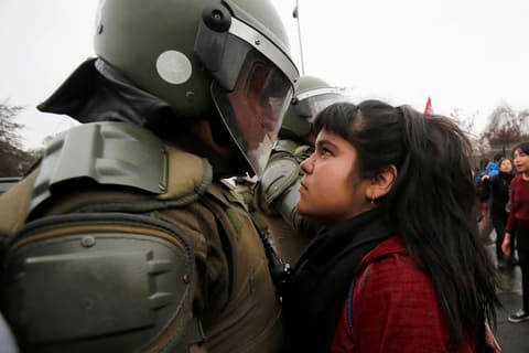 Image of young girl in Chile standing eye to eye with riot police. 