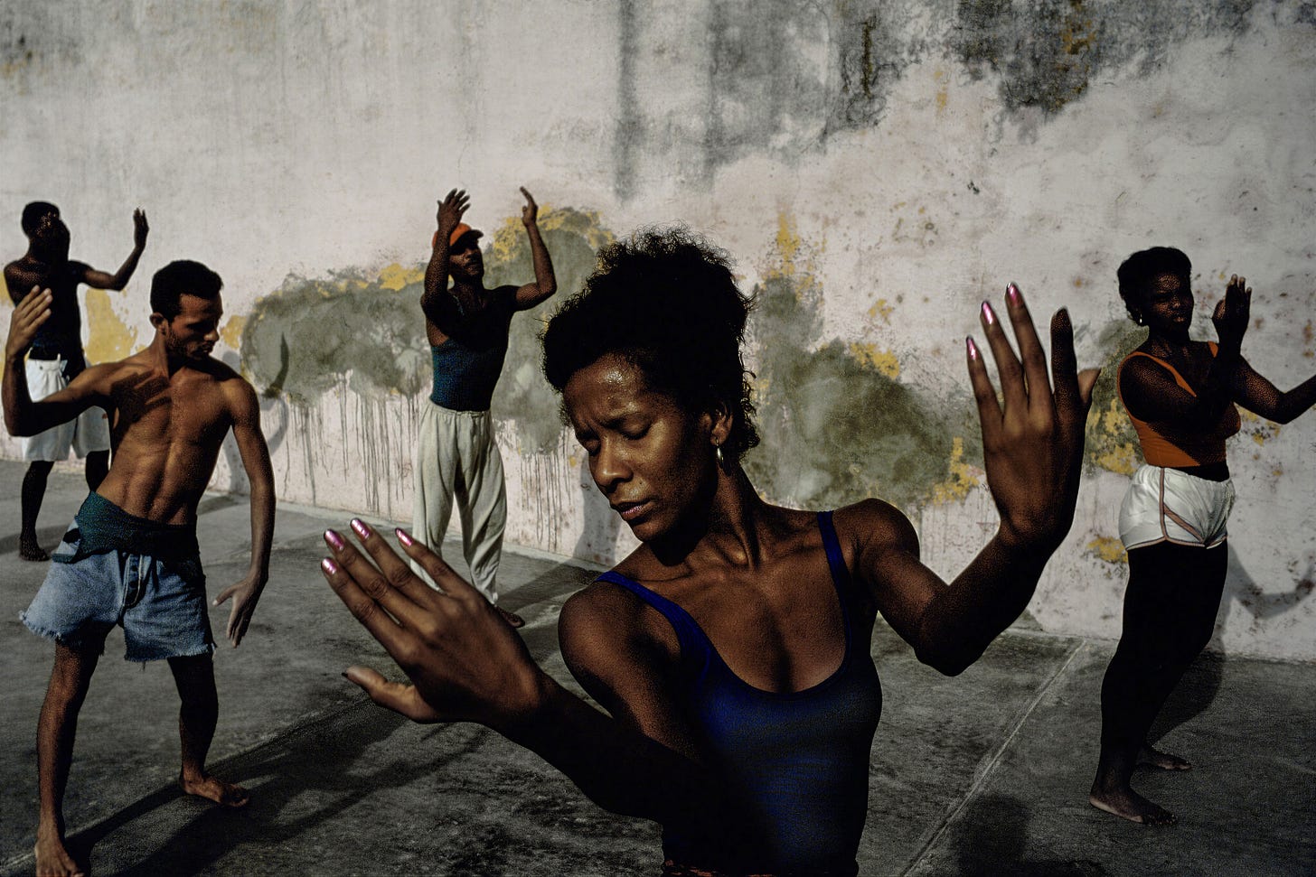 David Alan Harvey - Five people practice a dance or martial arts routine outdoors against a weathered wall. A woman in front leads with outstretched arms, while others mirror her movements, focused and expressive.