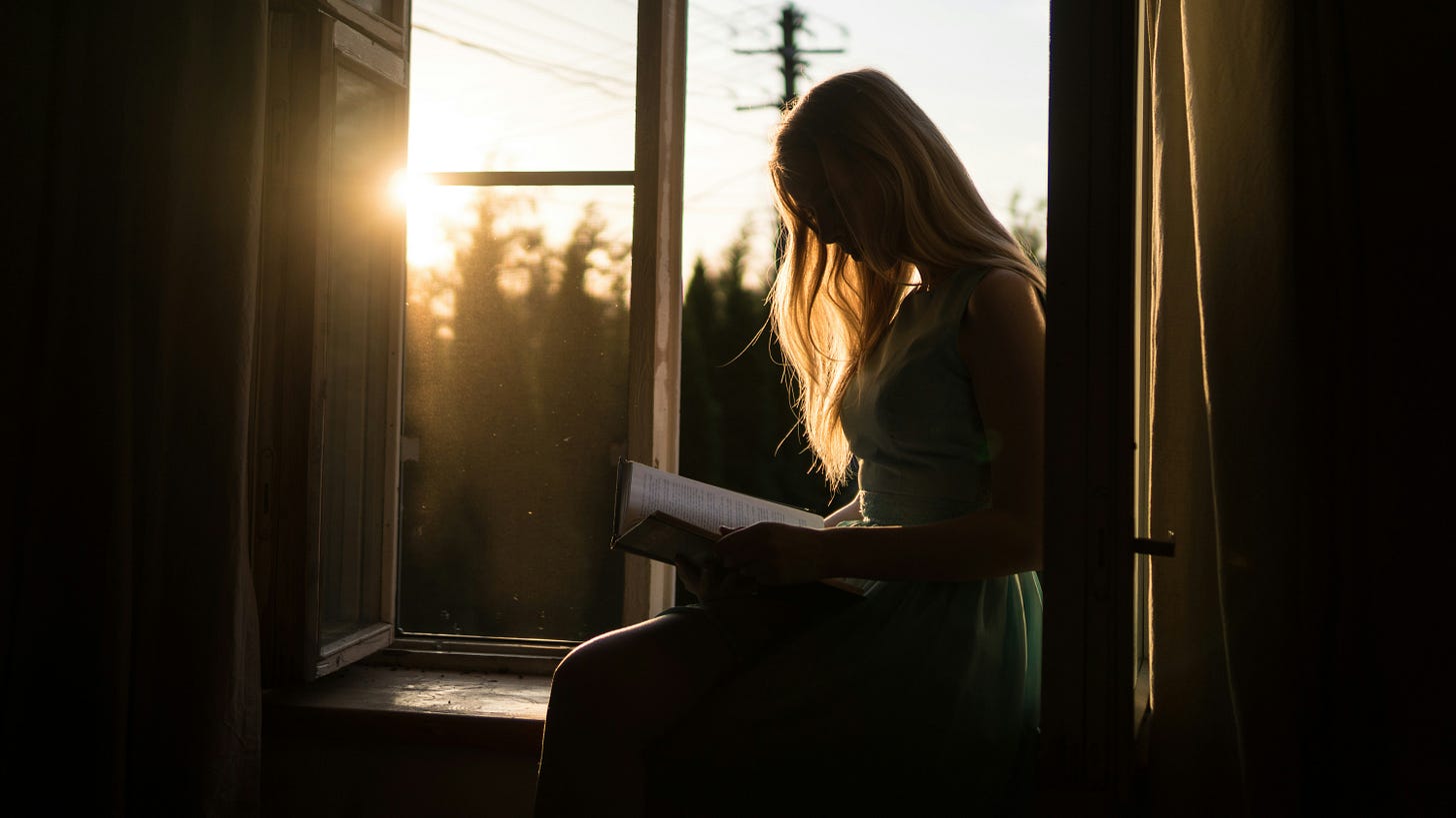 woman-reading-book-while-sitting-at-window