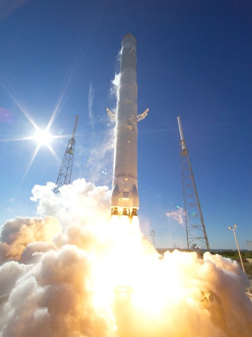 Free A powerful rocket takes off into a clear blue sky, surrounded by clouds of smoke. Stock Photo
