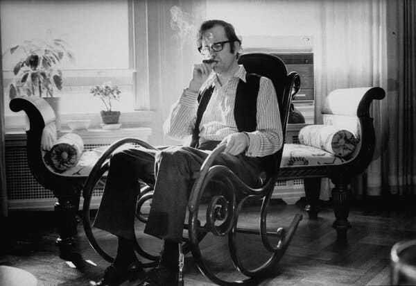 A man in an ornate rocking chair, smoking a cigar. He is wearing glasses, a striped shirt and a vest. A man in an ornate rocking chair, smoking a cigar. He is wearing glasses, a striped shirt and a vest.