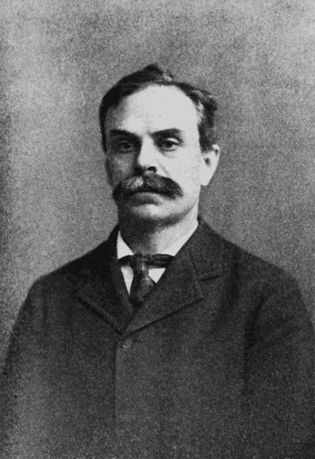 Portrait of Edwin Herbert Hall as a young man with a dark mustache, wearing a suit and tie, facing forward against a plain studio background.