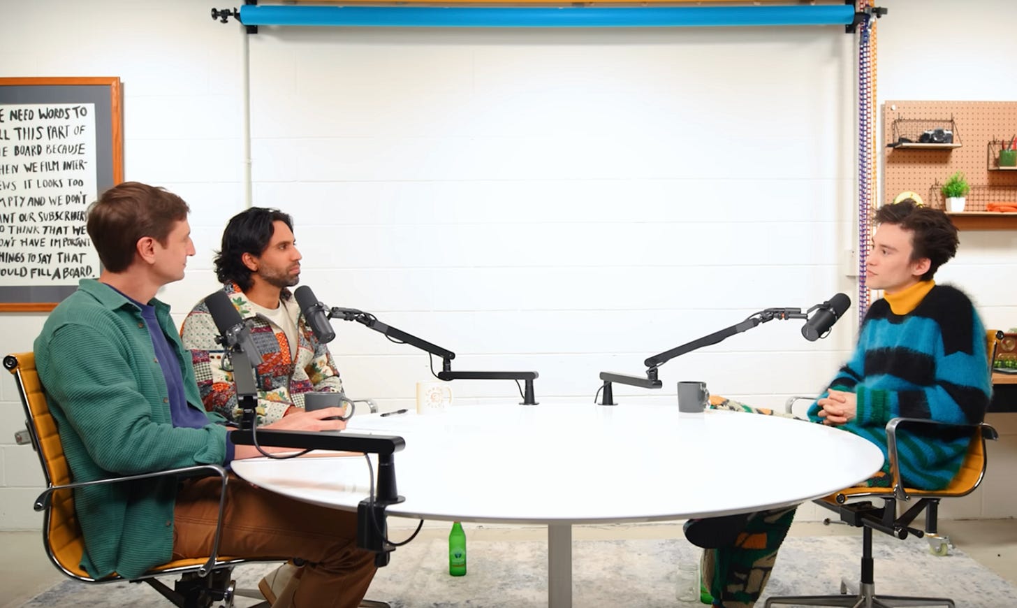 a screenshot of Colin, Samir, and Jacob sitting at a circular table with podcast microphones in a Youtube studio