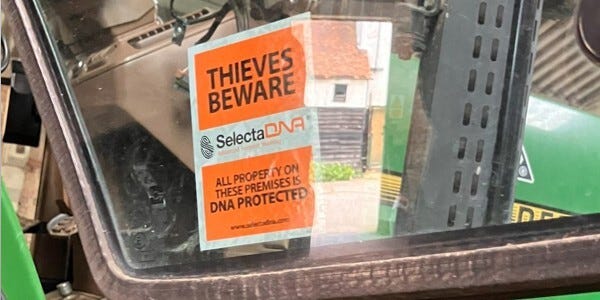 orange and white poster in Tractor window: 'Thieves beware - Selecta DNA - All property on these premises is DNA protected'