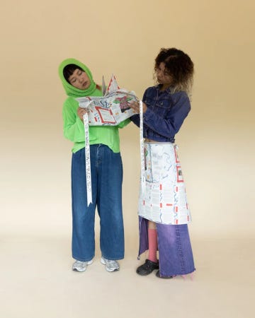 La même a remplacé sa chemise par un gilet. Elle tient maintenant la chemise, repliée comme un magazine, qu'elle montre à une amie