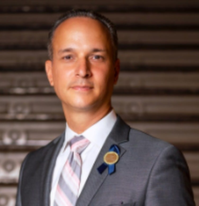dist 14 superintendent david cintron, in a suit against abackdrop of a metallic rolling garage door, staring at the camera; dist 14 superintendent david cintron, in a suit against abackdrop of a metallic rolling garage door, staring at the camera;