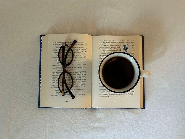 This may contain: an open book with glasses and a cup of coffee