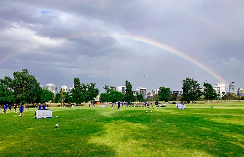 a rainbow framing a sports ground. there are kids training on the ground. a rainbow framing a sports ground. there are kids training on the ground.