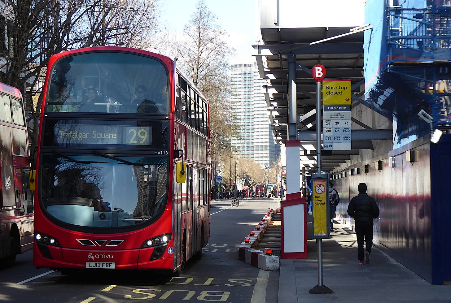 Number 29 bus heading south on Tottenham Court Road past a closed bus stop with steel gantry hanging over carriageway. Number 29 bus heading south on Tottenham Court Road past a closed bus stop with steel gantry hanging over carriageway.