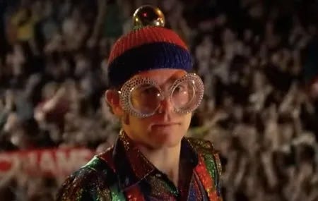 Elton John en grosses lunettes à diamant, bonnet en laine et chemise lulticolore dans le clip "I-Pinball Wizard", des Who