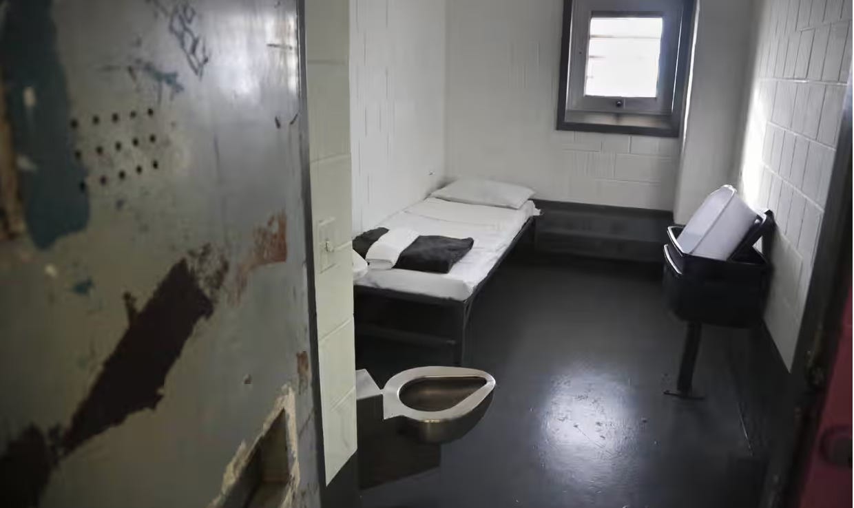 A small cell with a bed and a toilet shown