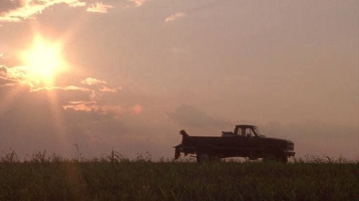 This may contain: a pickup truck is parked in a field with the sun setting behind it and two people sitting in the back